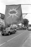 Close-up of Mohawk Warrior Society flag with view of truck being driven in front of a marching crowd on street 11 July 1995