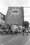 Close-up of Mohawk Warrior Society flag with view of marching crowd on the street being lead by drummers and singers 11 July 1995