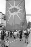 Close-up of Mohawk Warrior Society flag with view of marching crowd on the street 11 July 1995