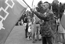 Close-up profile view of man in camouflage jacket holding a Haudenosaunee Confederacy flag tied to a branch 11 July 1995