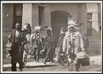 [First Nation chiefs carrying bags and briefcases gathered on field] 1909