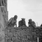 Studying map and Jerry-locations from castle ramparts, L to R: Lieut. J.P.S. Amoore, British Intelligence Corps, (Interpreter) attached to 1 Cdn. Div.; Brig. M.C. Vokes, (2 CIB Brigadier) Lt.-Col. G. Kitching, Staff Officer 1 Cdn. Div 1943