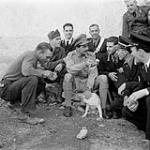 Pte. I.D. Leroux released by Italians after 15 months internment in Italy after capture at Tobruk, reached Melfi and was greeted by British and Canadian troops. His six companions were shot moving through Jerry lines. Shown is Capt. K.A.F Horby, assorted Italian police and "Lulu" the Italian police pet which Jerry stole in his retreat but which escaped to return to barracks a day later (also an escaped prisoner). One of the police is ex-P.O.W 1943