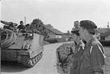 Fallex 77. Capt. Gendron, 2 R22eR, and Major Bursall, NDHQ, umpires for Ex. Carbon Edge, watch a 1R22eR armoured personnel carrier pass through a village September 1977.