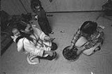 [Kenojuak Ashevak eating seal with Inuk woman and baby] December 1980