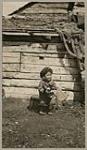[Inuk toddler in kamek/kamiik (sealskin boots) and fur hat holding a sled dog puppy] [between 1920-1922]
