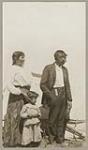 [Anishinaabe woman, man, and girl standing in front of tent] 1920