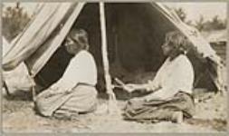[Two seated Anishinaabe women while making a net. The woman on the right is holding a netting needle] 1920