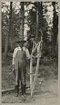 [Anishinaabe man displaying snowshoe frames that have been bent and secured for drying] 1920