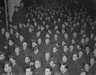 Eager to step foot in the United Kingdom, this big draft of aircrew trained by the RCAF in the British Commonwealth Air Training Plan throng the deck of their transport, listening to words of welcome by Air Commodore T.E.B. How (OBE, AFC, and Bar), on arrival overseas [1940-1945].