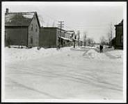 [Man shovelling sidewalk of snow-covered residential street] [1927-1932].
