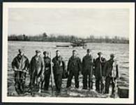 [Group of workers holding tools at water`s edge with floating barge in background] cira 1924-1928.