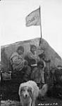 Autochones, côté nord-est, Île de Baffin, T.N.-O. [De gauche à droite : Uuttuvak, Tuurngaaluk, Uuttuvak Kinngilik et un garçon inconnu. Moses Ittukusuk figure en avant plan avec Loonie, le chien de la Compagnie de la Baie d'Hudson. La photographie a été prise à l'extérieur de la maison d'Akumalik, comme l'indique le drapeau.] 17 Sept. 1924