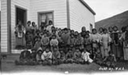 Pangnirtung natives, at Mission House, Baffin Island, N.W.T., ca. 1927 [Standing on the steps: Saimmaiyuq (second from the left) and Tatiggaq (fourth from left in front of the window). First row standing: Aluki (fifth boy from left in centre of row) and Aittainnaq is near the far end (third woman from the right)] 1927