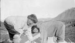 Pouring insulation material on roof of Doctor's House. Pangnirtung, Baffin Island, N.W.T. October 1928. [Veevee (left) and his grandson Pauloosie Veevee (right) repairing a boat.] Octobre 1928