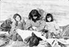 Inuit woman sewing, accompanied by two children 1949