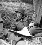 Brigade Major Geoff Boone (Toronto, Ont.) of 8th Brigade reads newspaper during German shelling 06-Jul-44