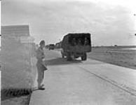 Gunner H.E. Robertson on guard duty as a convoy of German vehicles crosses the Zuiderzee causeway en route to Germany. Netherlands, 27 May 1945 May 27, 1945.
