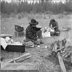 On the way to the Quesnel, B.C., cattle sale, Pan Phillips drinks a mug of coffee while his wife Betty cooks a stew over the gas stove, and baby Robert enjoys his thumb Oct. 1956