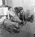 Able Seamen Garth Barnes and Paul Kuzma relaxing during a lull in action stations aboard the cruiser H.M.C.S. UGANDA in the Pacific Ocean, 18 May 1945 May 18, 1945.
