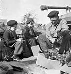 Trooper E.T. McConnell of the Calgary Regiment is watched by Belgian boys as he opens packages of tank parts as the regiment re-equips with Sherman Vc Firefly tanks, Dottignies, Belgium, 25 March 1945 Marh 25, 1945.