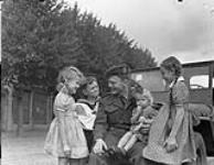 Private Murray Dorey of the Canadian Army Occupation Force (C.A.O.F.) giving chocolate to German children, Aurich, Germany, ca.26-27 August 1945 [ca. August 26-27 1945].