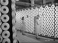 Des ouvrières, à la manufacture de textiles de la Montreal Cottons, ajustent des fusettes (« fromages ») de fil de coton embobiné très serré vers mars 1942