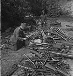 A German sergeant, under guard, checks piles of automatic weapons 18 May 1945