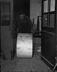 Printing first issue of the Maple Leaf in Caen. Pte. Rolland Smith wheeling a roll of paper for the press 28-Jul-44