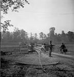 Military policeman directs traffic of the Stormont Dundas and Glengarry Highlanders across a Bailey bridge over the Orne River built by Royal Canadian Engineers 18-Jul-44
