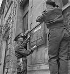 Lt.-Col. R.S. Malone helping to erect sign for the Canadian Maple Leaf Editorial Offices 11 July. 1944