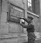 Capt. Placide Labelle adds notice on the sign for Canadian Maple Leaf Editorial Offices 11 July. 1944