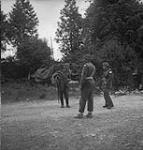 A prisoner of war with guards in the yard of the house occupied by the 8th Brigade 10 July. 1944
