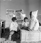 Inuit children with supplies for the Roman Catholic Mission landed from the Eastern Arctic Patrol vessel C.G.S. C.D. Howe. [Jaimisi Piugaattualuk (left), Maata Miqqusaaq (center) and unidentified individual (right) seen resting from unloading "sealift" supplies for the Roman Catholic Mission.] 1 Juillet 1951