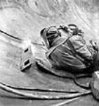 Workman wearing welder's mask welds seam of a tank to be used for chemical storage in the Polymer Corporation Limited plant juin 1943
