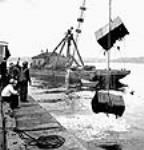 Cases of salvaged goods being lifted from a sunken freighter out of the water July 1943