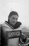 Young woman holding a small chalk board with the number 6010 at Pond Inlet (Mittimatalik/Tununiq), Nunavut, August 1945. [She has been identified as Juunaisi and also Eunice Kunuk Arreak]. August 30-31, 1945.