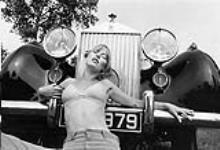 Woman modeling underwear is posed on the hood of a car 1972