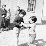 Two young Inuks play fighting with three young Inuit women watching on, Baker Lake (Qamanittuaq), Northwest Territories [Nunavut], 1948. [The late David Annanaut is the boy on the right, the woman in the centre is the late Marjorie Esa and the woman on the right is Ruth Tulurialik.] 1948.