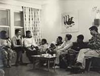 [Group of people [Left to right: ?, Alma Houston, Surusilutuq Ashoona, Annie Pootoogook, ? Shooyoo Pootoogook, Barbara Hinds, Kananginak Pootoogok, Eegyvudluk Pootoogook] sitting in a room, Kinngait, Nunavut] [between 1956-1960]