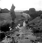 [Sarpinak (right) and Mosha Michael (left) standing by a stream with a bucket] [between 1956-1960]