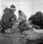 [Mackenzie Porter (left), a boy, and Kiakshuk (right) sitting in a tent, Kinngait, Nunavut] [between 1956-1960]