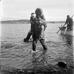 [Mackenzie Porter carrying Barbara Hinds to shore on his back, Iqaluit, Nunavut] 1960