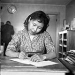 [Woman writing at a desk, Iqaluit, Nunavut] 1960