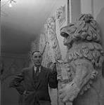 William Oosterhoff prenant une pose avec des masques et une sculpture [ca 1954-1963].