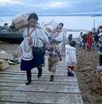 Femmes [Au premier plan: Tipansie Kilabuk, Natsiva Kilabuk, Mary Kilabuk, Annie Pisuktie, en arrière-plan: Shuvinai Mike et Kootookuluk Mitsima] déchargeant des sacs de sucre d'une barge de la Compagnie de la Baie d'Hudson à Apex, baie Frobisher, T.N.-O., [Iqaluit (anciennement baie Frobisher), Nunavut] [between June-September, 1960].