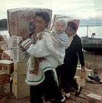 Femmes [Susie Kaivaluaqjuk, et Haaila Nuqinggaq ou Haaila Newkinga] déchargeant des sacs de sucre d'une barge de la Compagnie de la Baie d'Hudson à Apex, baie Frobisher, T.N.-O., [Iqaluit (anciennement baie Frobisher), Nunavut] [between June-September, 1960].