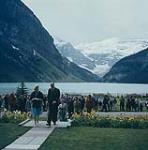 Queen Elizabeth II accompanied by the manager of the Chateau Lake Louise, approaching the entrance to the Chateau. Lake Louise and Victoria Glacier are in the background.  juillet 1959