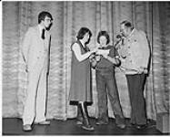 CKWS'S Gary Mercer on stage with a microphone. Two women are reading a piece of paper and another man looks on December 22, 1978