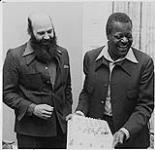Portrait of Oscar Peterson upon receiving a cake. Jack McAndrew (?) stands next to him [between 1970-1980]